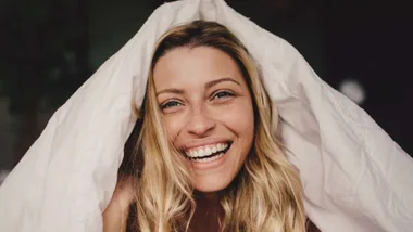 Woman smiling with duvet cover over her head like a hat