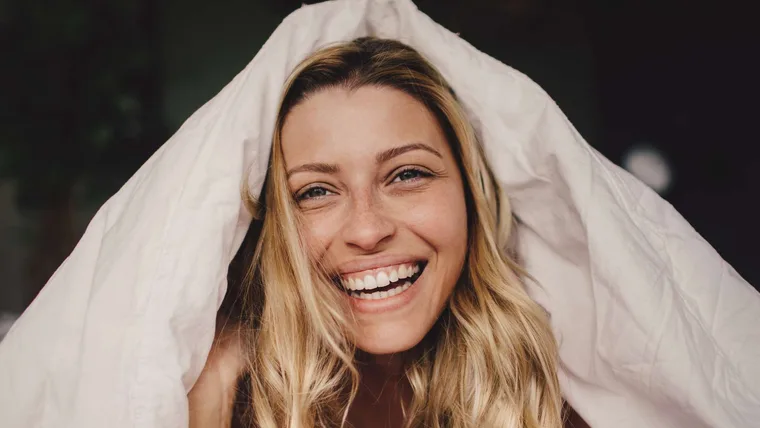 Woman smiling with duvet cover over her head like a hat