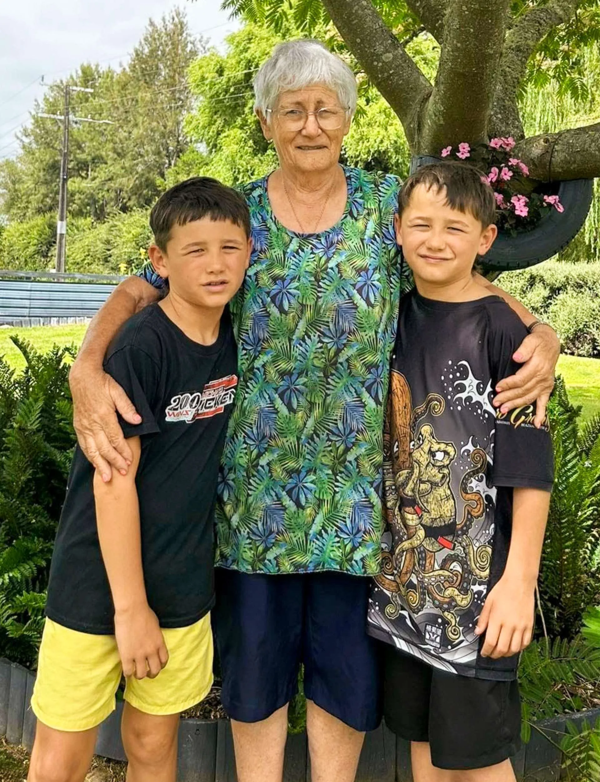 Jenny-May's sons standing on either side of their grandmother in front of a tree