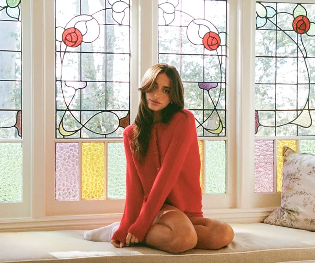 Woman in a red sweater sitting on a bench in front of ornate stained glass windows.