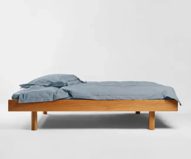 A wooden platform bed with blue sheets and pillows against a white background.