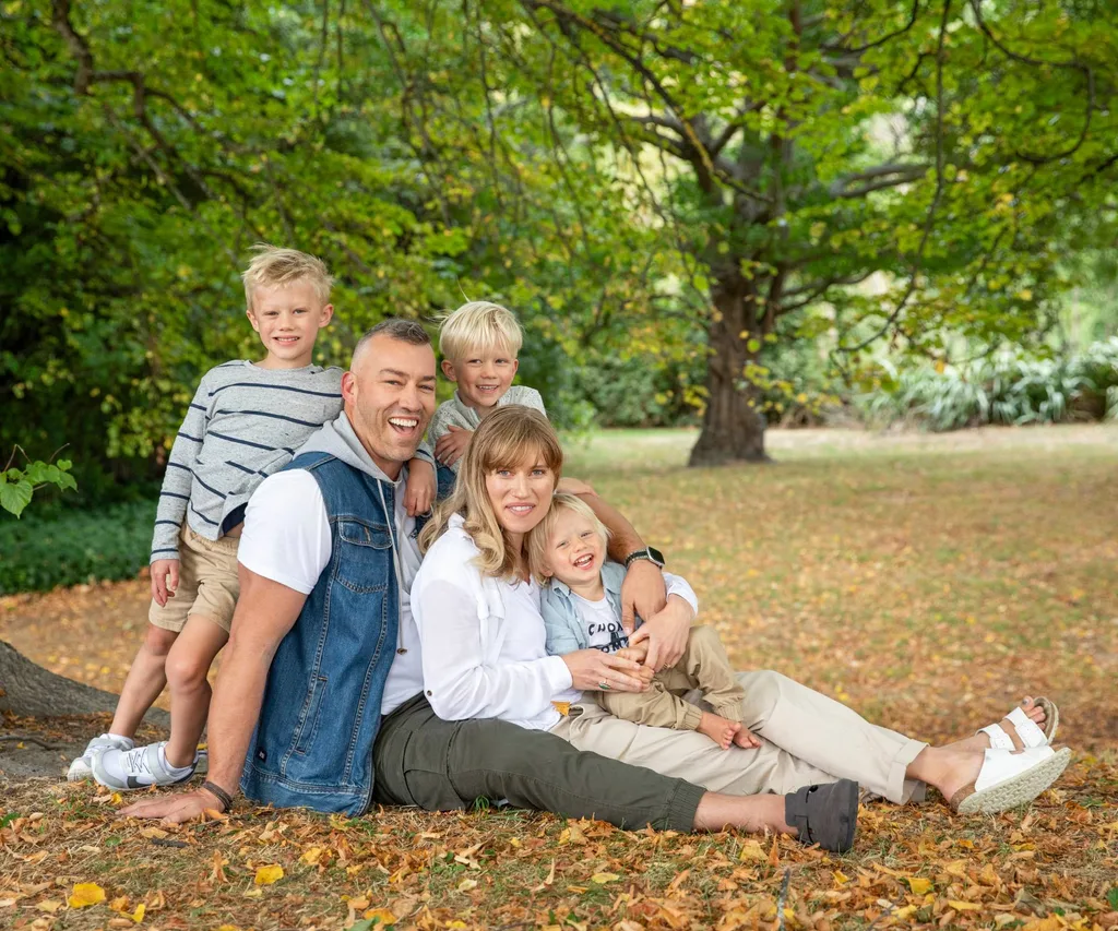 A family photo of Aaron and Emma sitting under an autumnal tree with their sons around them