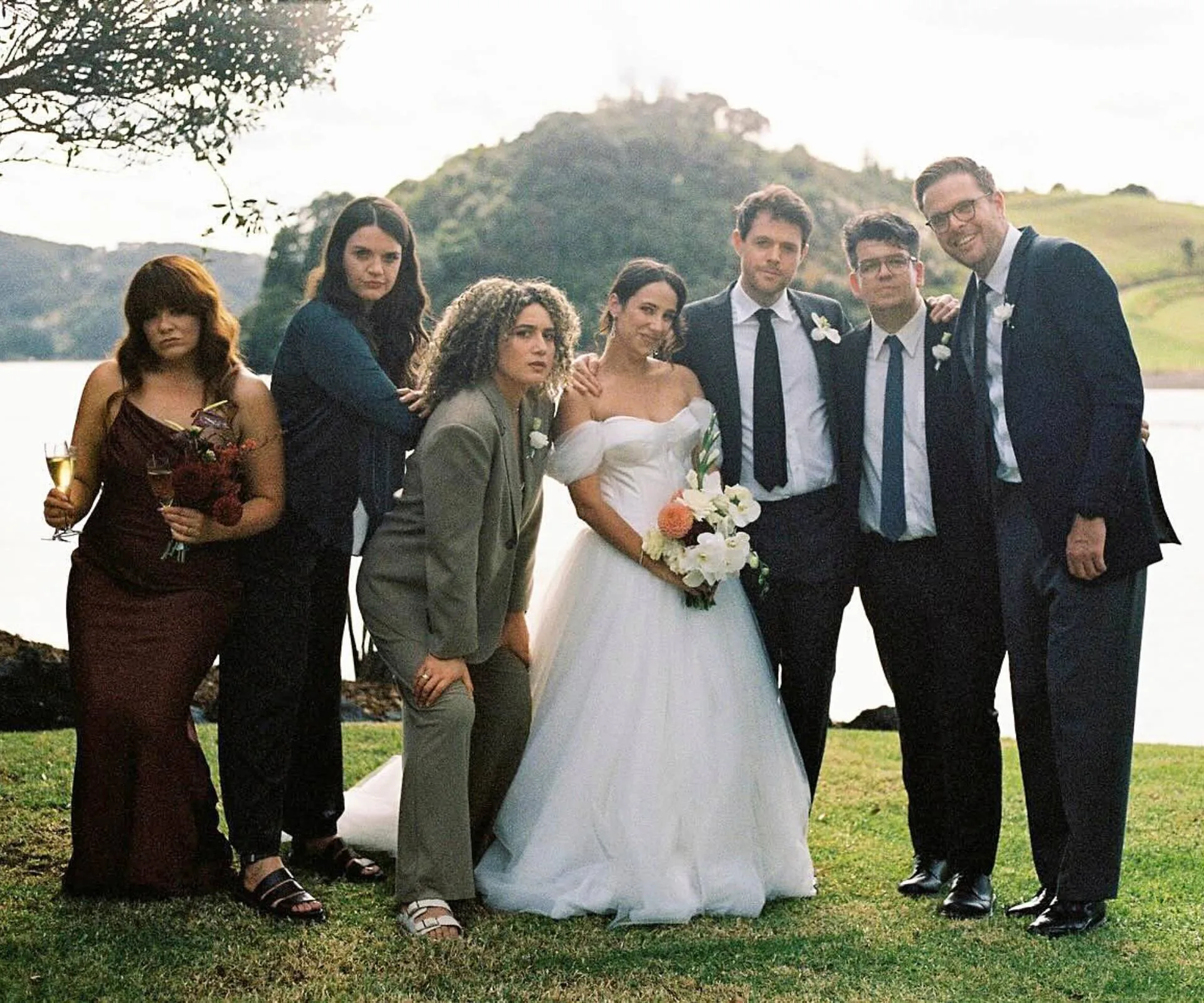 Simone and Guy at their second of two weddings, with their bridal party around them in front of a lake