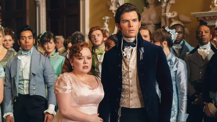 A group of people in elegant Regency-era costumes gathered indoors, looking attentively forward.