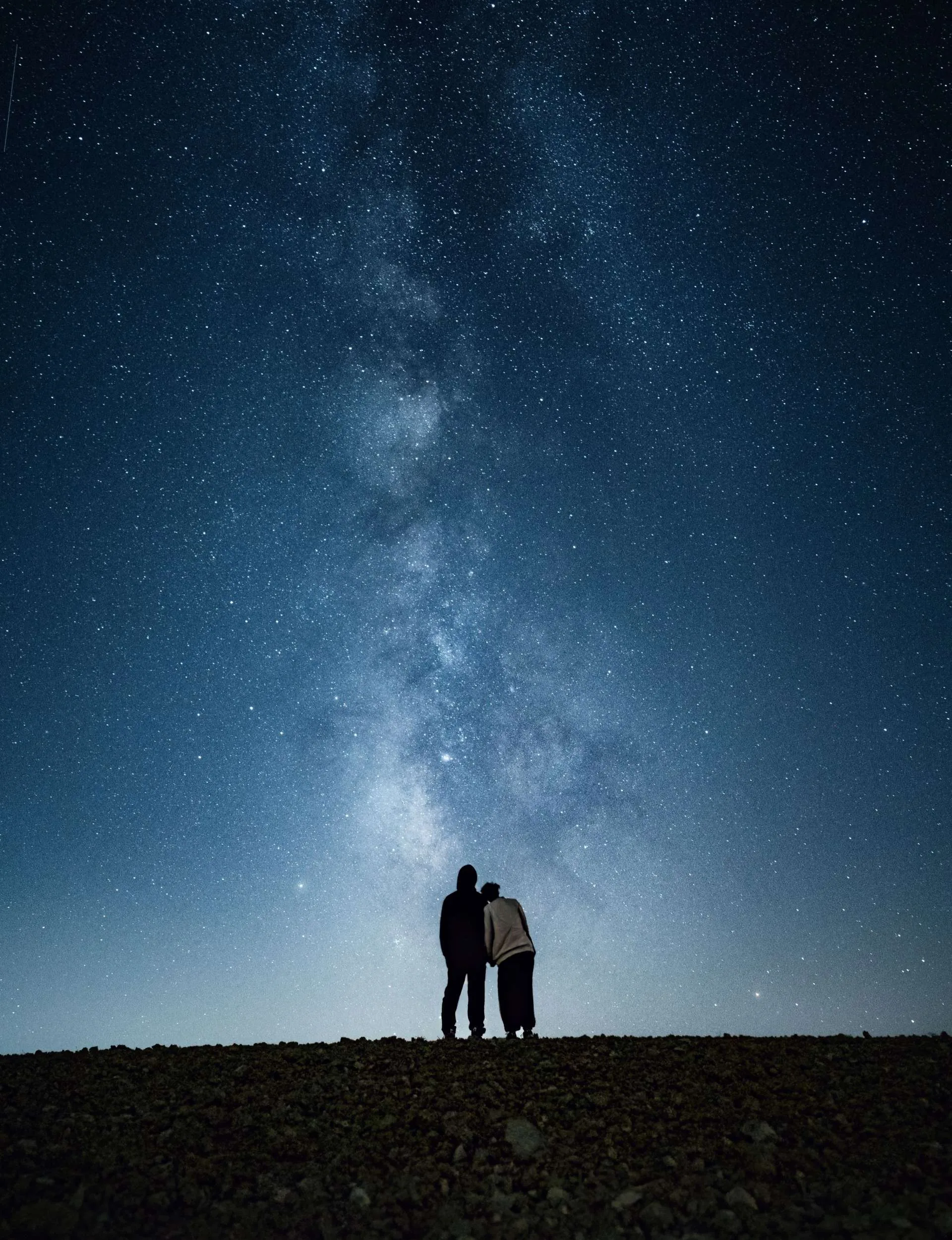 Silhouettes of two people standing on top of a hill looking at the stars