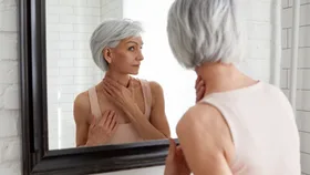 Woman applying skincare to her neck while looking in a black framed mirror
