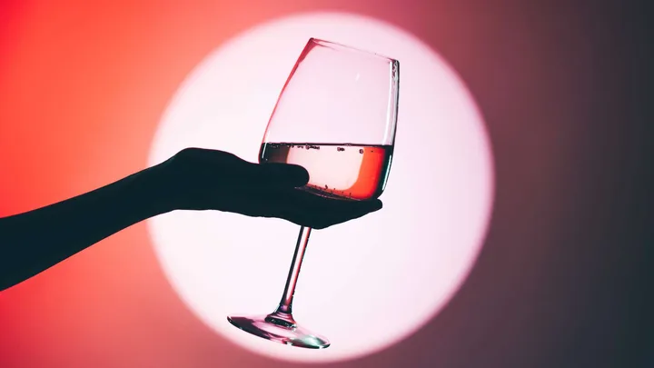 A hand holding a wine glass in a spotlight