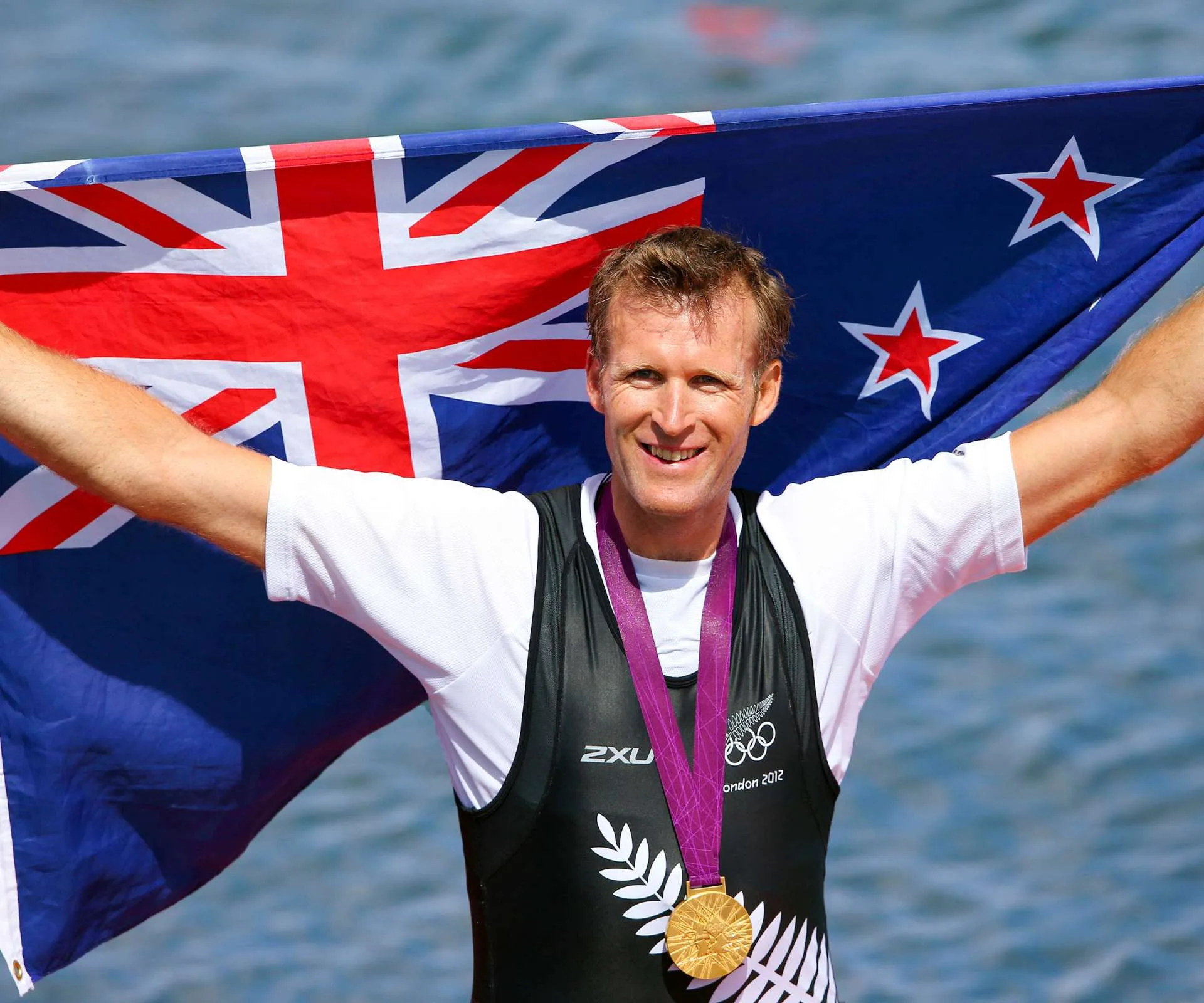 Mahé Drysdale holding a New Zealand flag with a medal round his neck after his Olympic win
