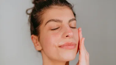 Woman rubbing cream on her face to sooth her Rosacea