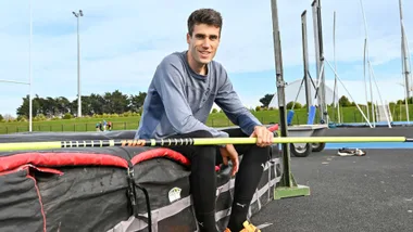 Hamish Kerr sitting on a high-jump mat with the pole across his lap