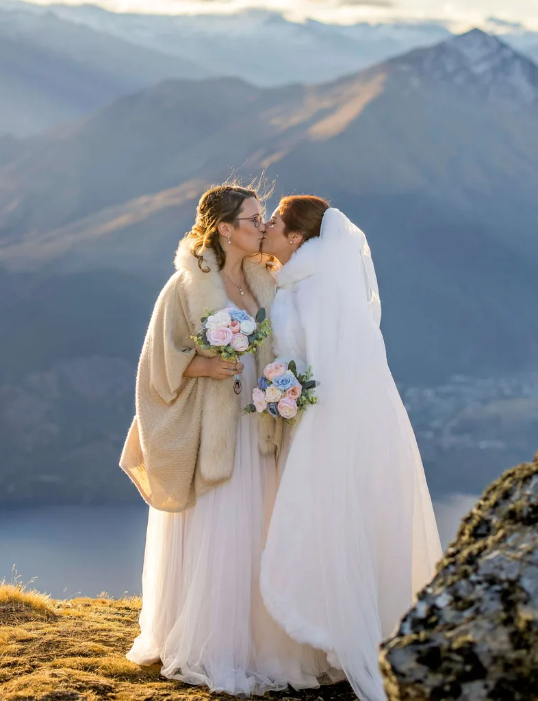 Melanie and Leah kissing on the mountain top in their wedding dresses