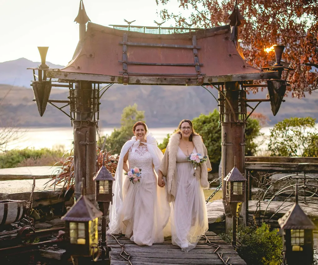 Melanie and Leah walking under a temple-like structure in their wedding dresses