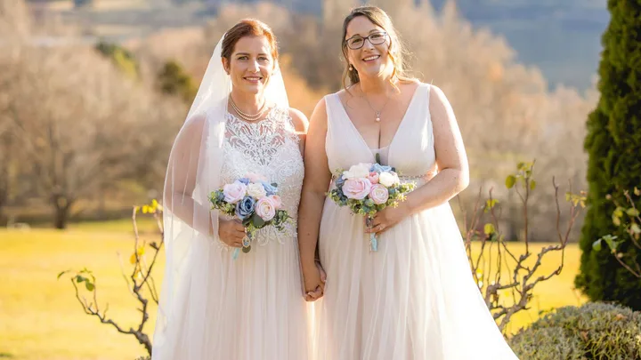 Melanie and Leah holding hands in their wedding dresses with their bouquets