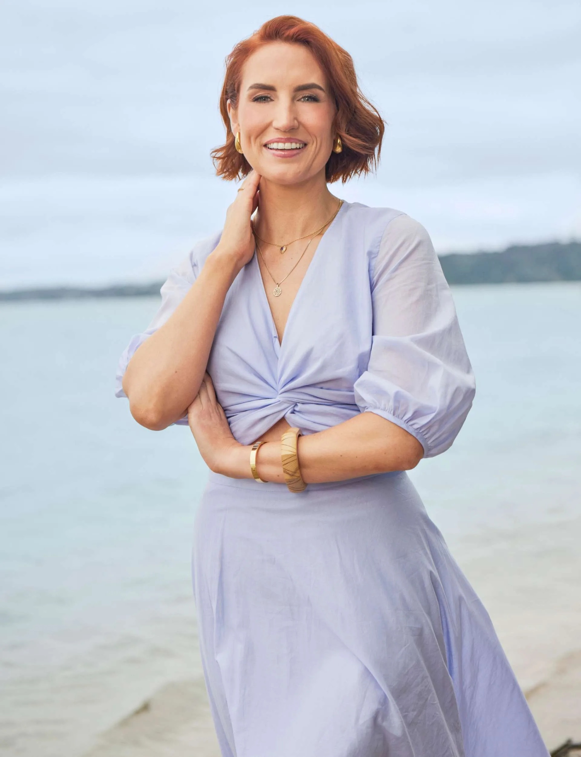 Sam Hayes smiling at the camera with one arm across her stomach and the other hand around her neck