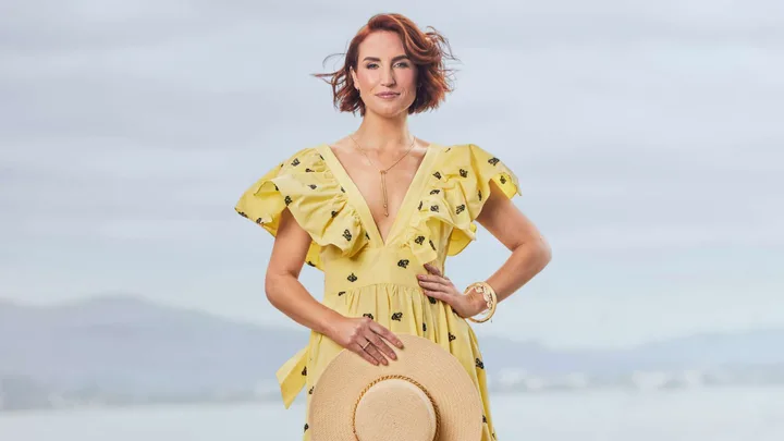 Samantha Hayes in a yellow dress holding a sunhat on a beach