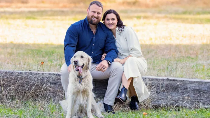 Tom and Dana Walsh sitting on a wooden beam with dog Rippa