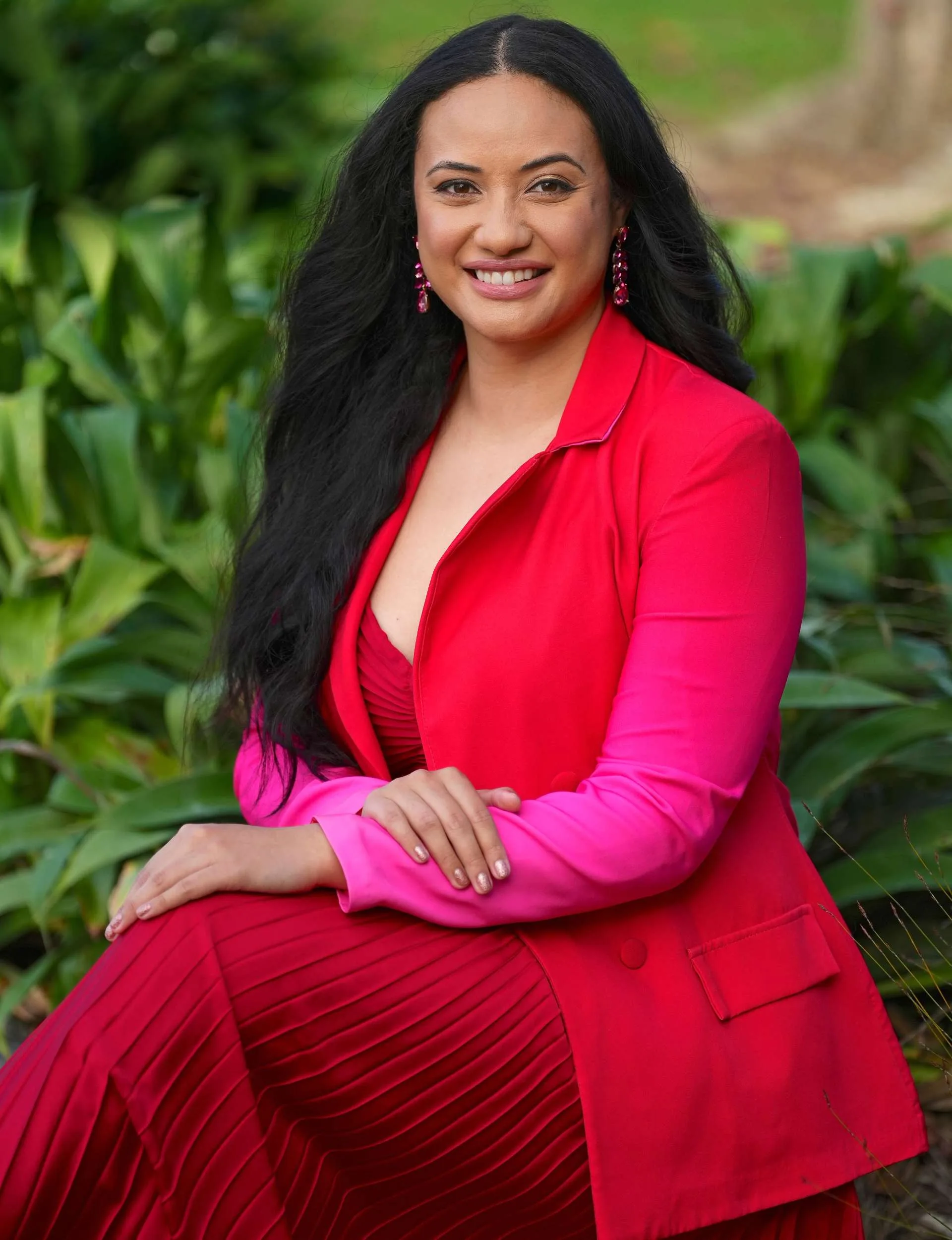 Sitting pretty in a red blazer and skirt in front of greenery