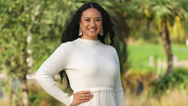 Diamond Langi in white in front of some trees with one hand on her hip