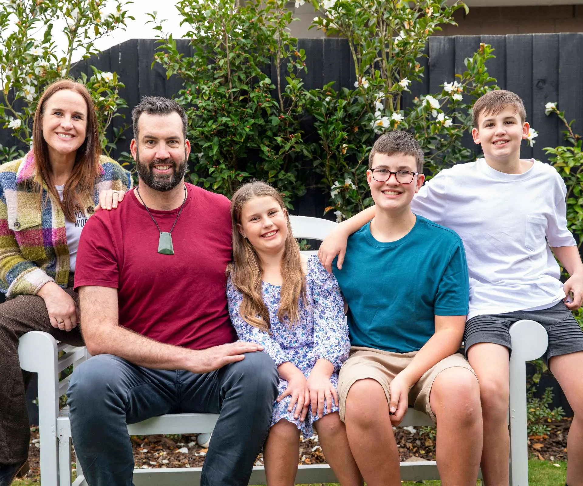 A family photo of Jay and Nicky with their three kids sitting on an outdoor bench
