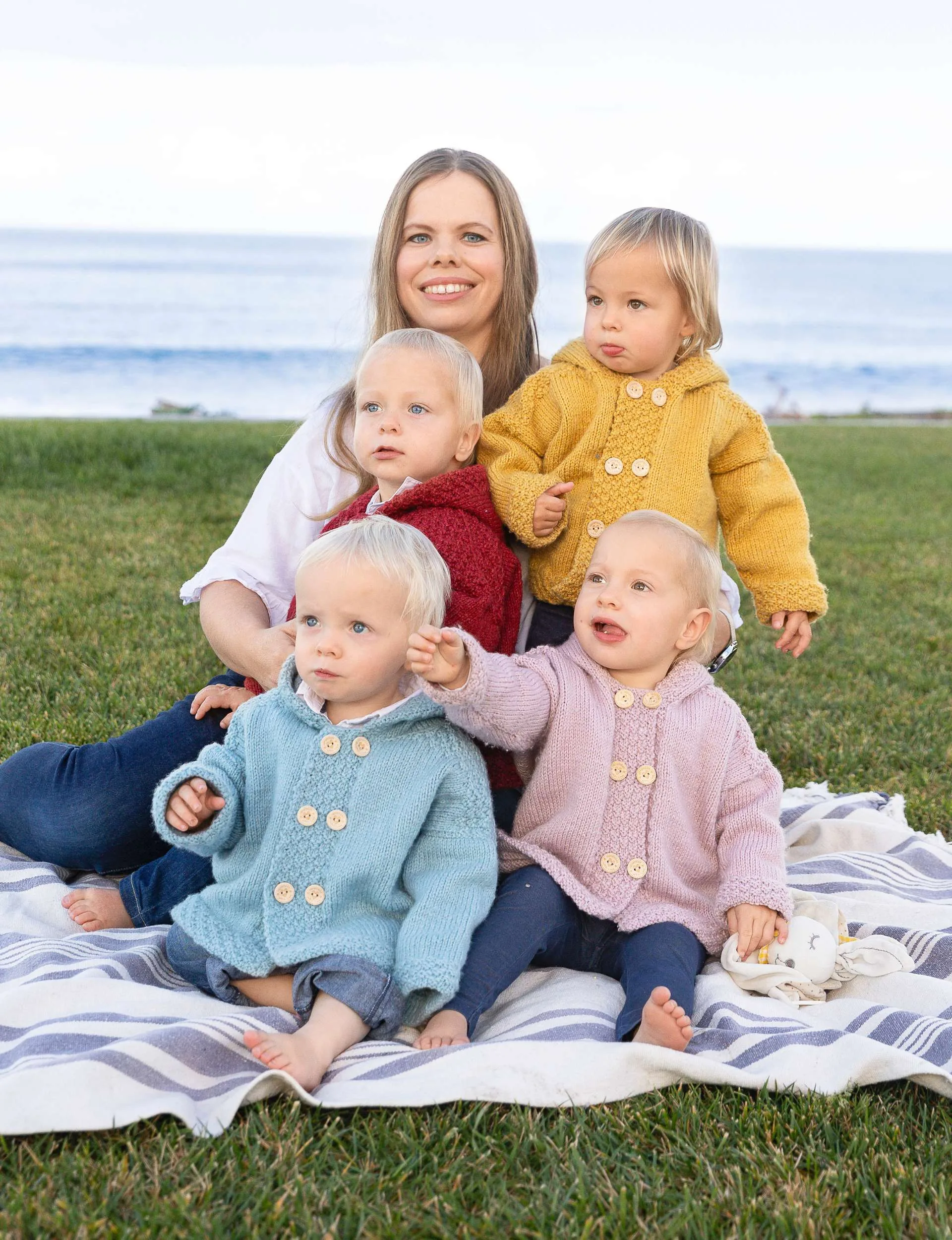 Joanne sitting on a patch of grass in front of a beach, with her children sitting around her