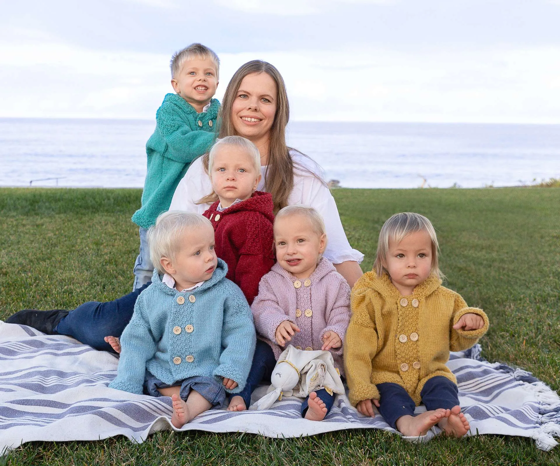 Joanne sitting on a patch of grass in front of a beach, with her children sitting around her