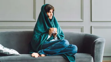 Woman sitting under a blanket on the couch with a warm mug