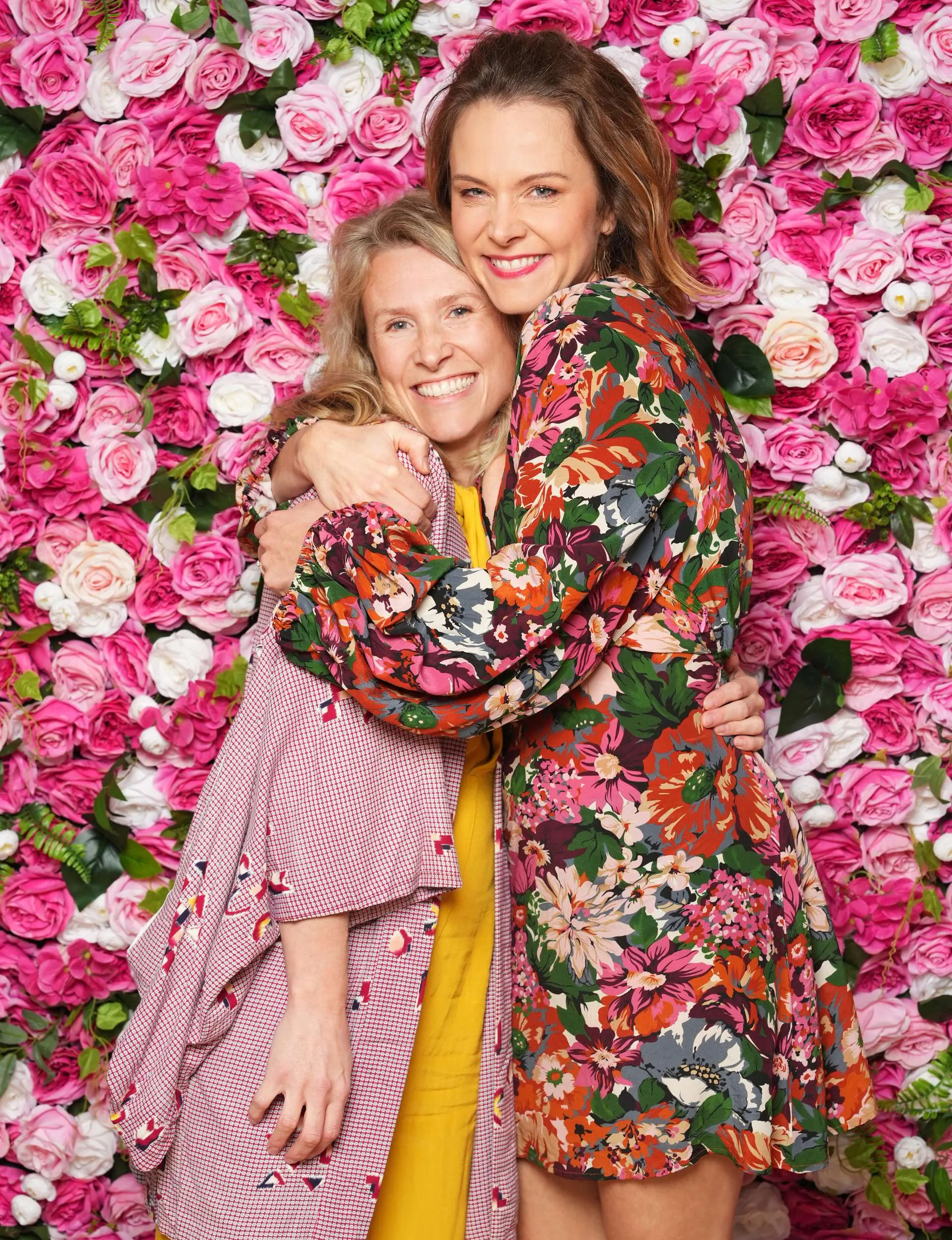 Big hugs from Ria to sister Zina in front of a flowery photo wall