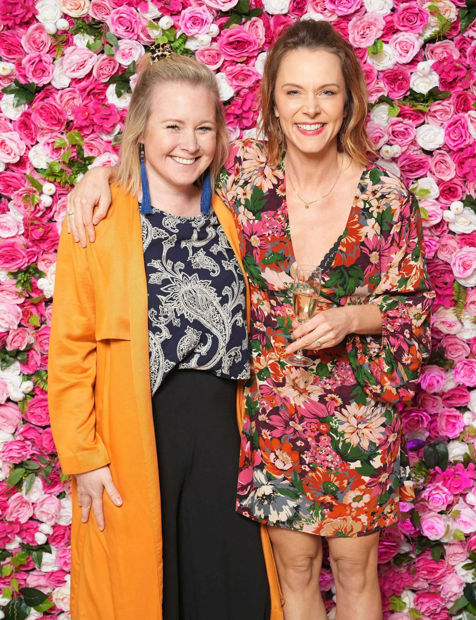 Ria Vandervis and Shorty co-star Sally Martin in front of a flowery photo wall