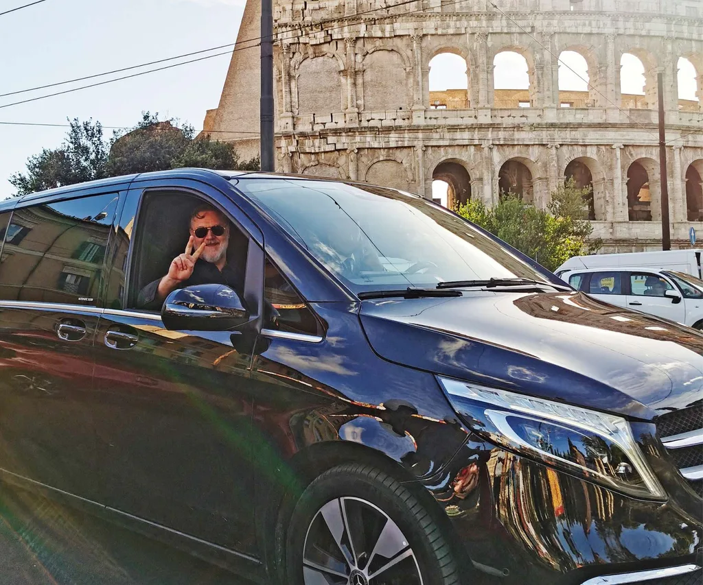 Russell holding a peace sign out of a black car window in front of the colosseum