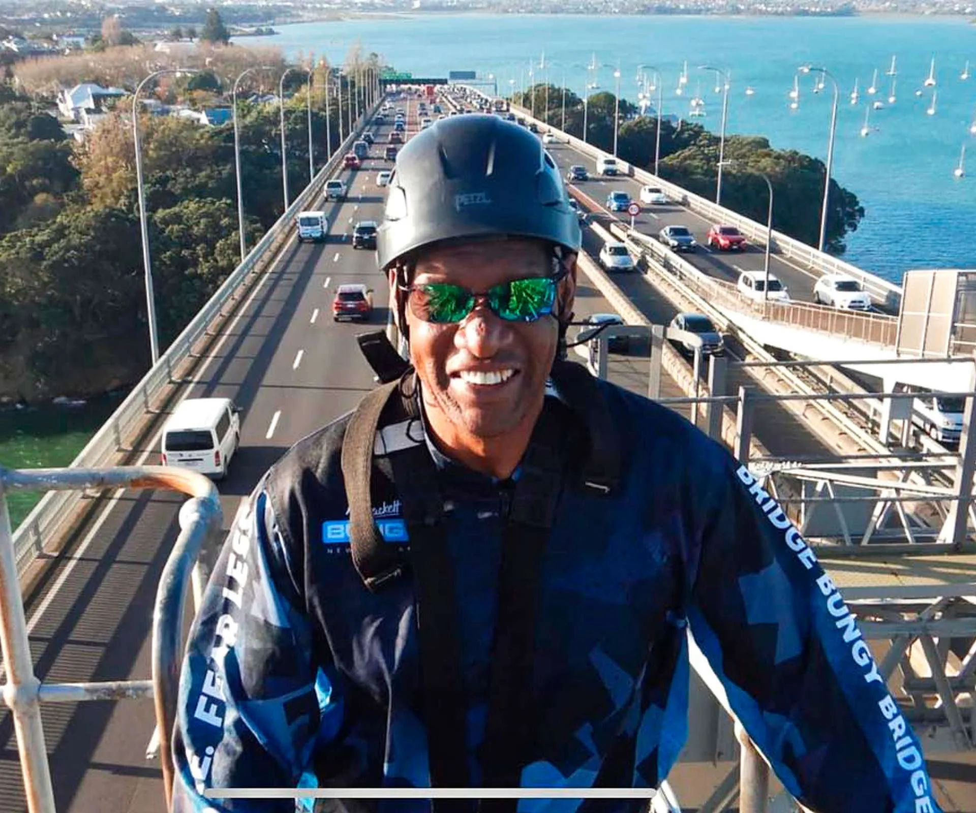 Shaun Wallace standing on top of the Auckland harbour bridge with cars whirring past below him.