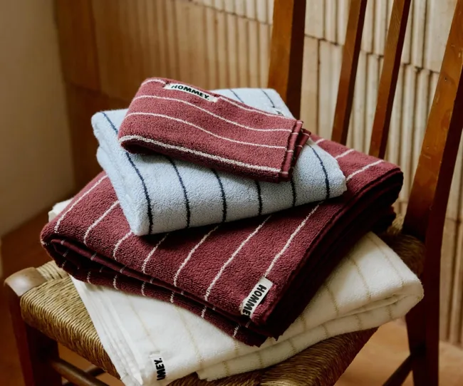 Stack of folded striped towels in burgundy, light blue, and white on a wooden chair.