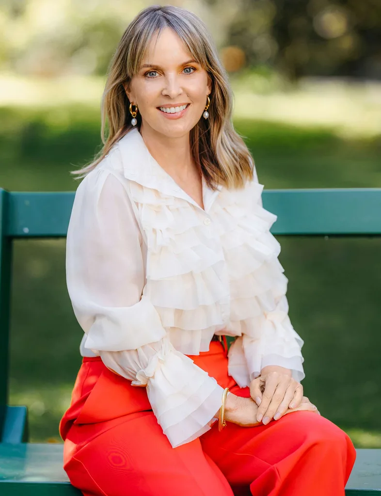 Angela in a white top and red pants sitting on a park bench