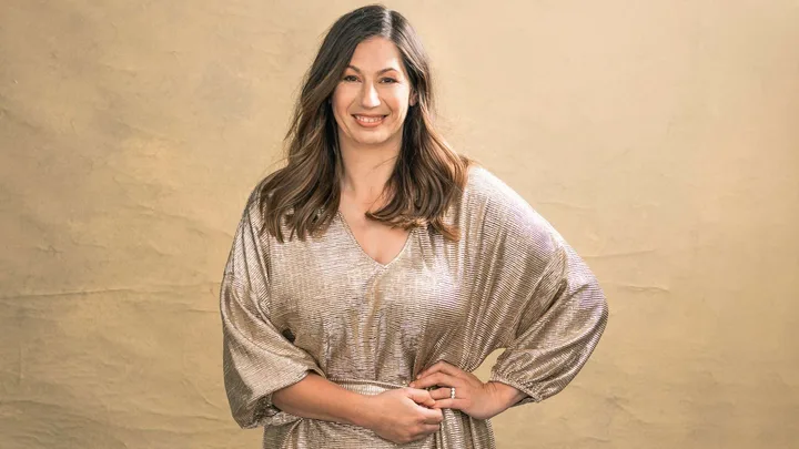 Emma-Kate Woodham in front of a gold background, wearing a gold dress