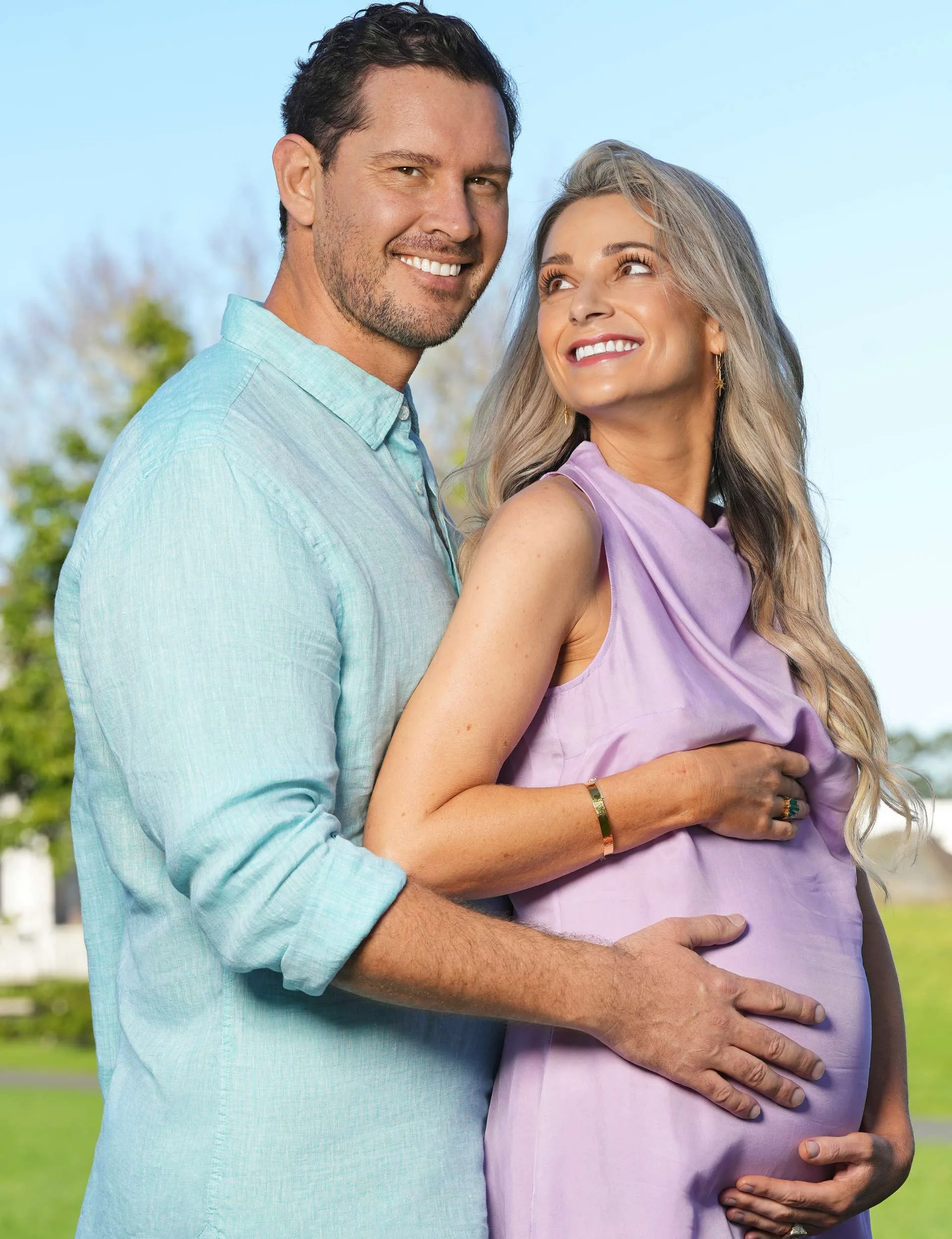 Erin standing in front of Zac, looking over her shoulder up at him, he has his arms around her and his hands on her stomach