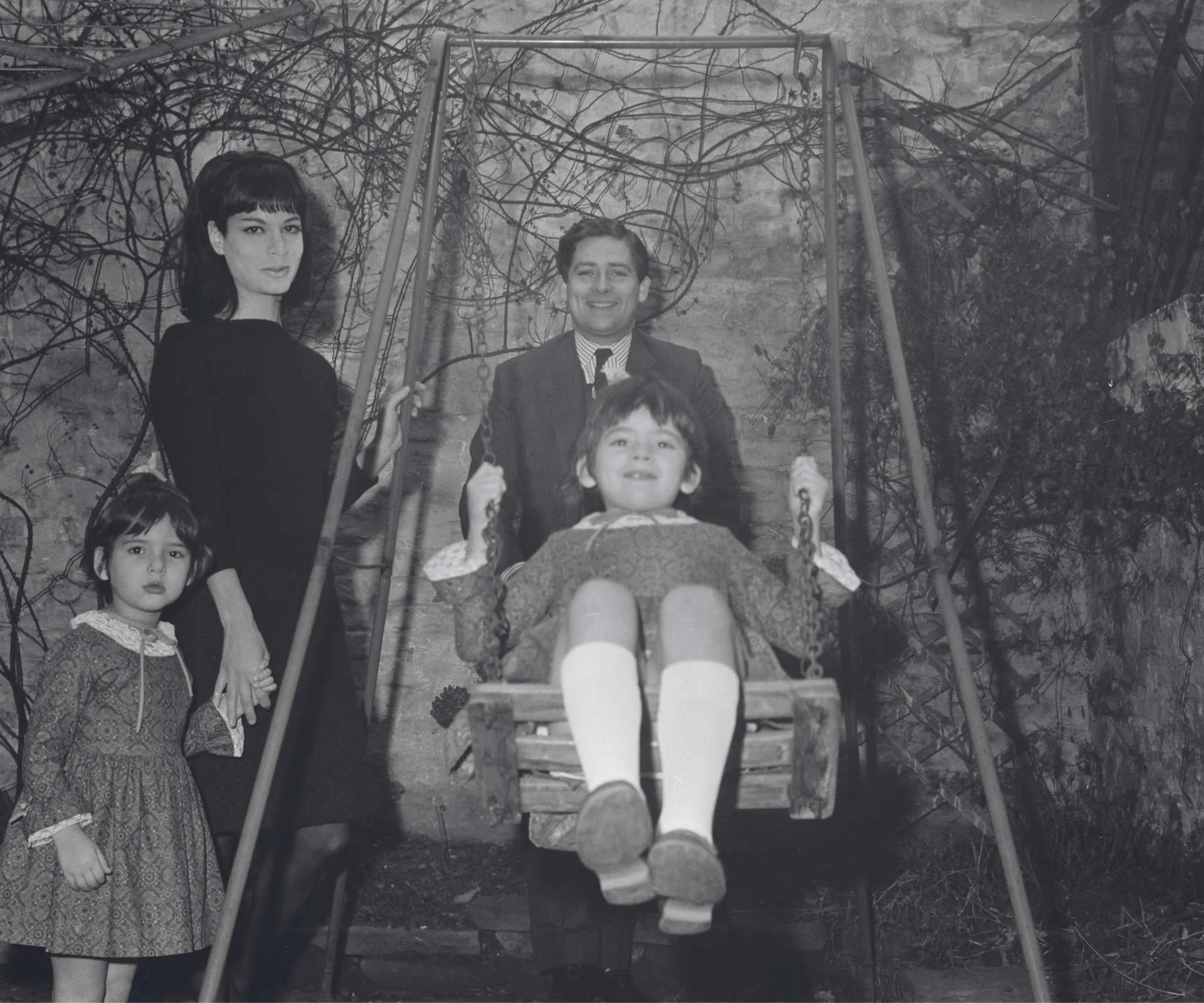 A black ad white photo of Nigella as a kid, swinging on a swing with her family
