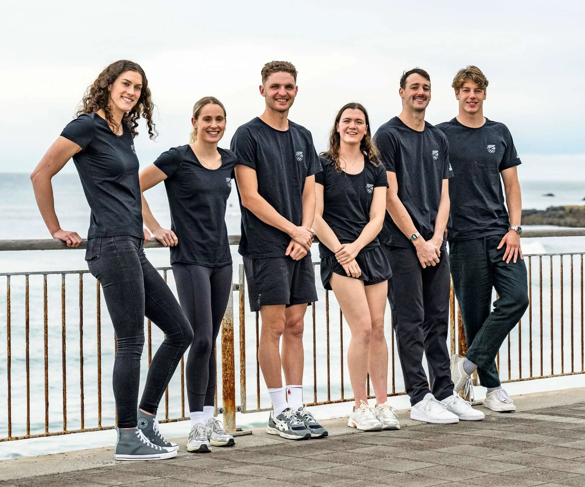 The Team New Zealand swimmers that will be competing in the 2024 Olympics all leaning on a rail in front of a beach