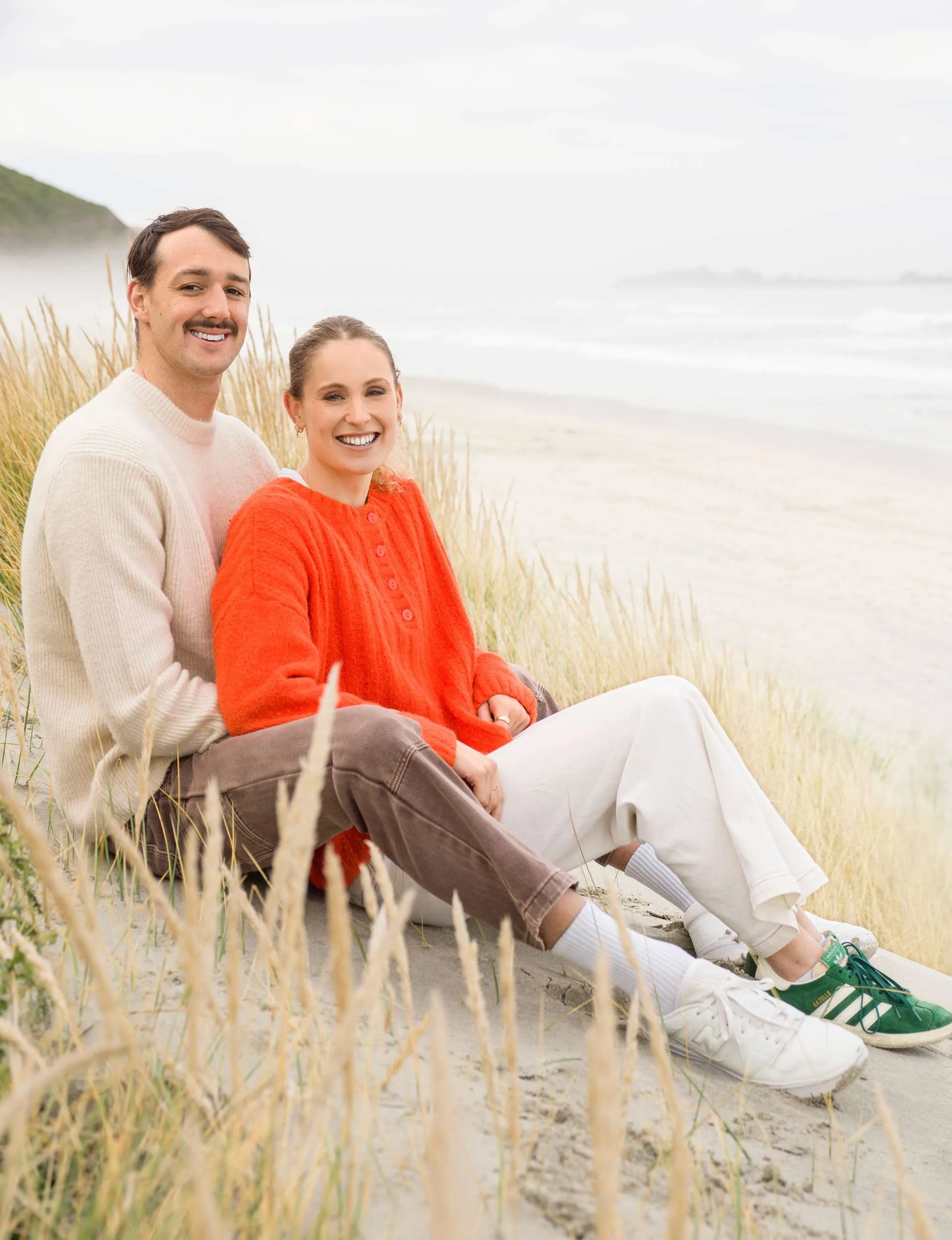 Caitlin sitting between Kane's legs on a sand dune at the beach