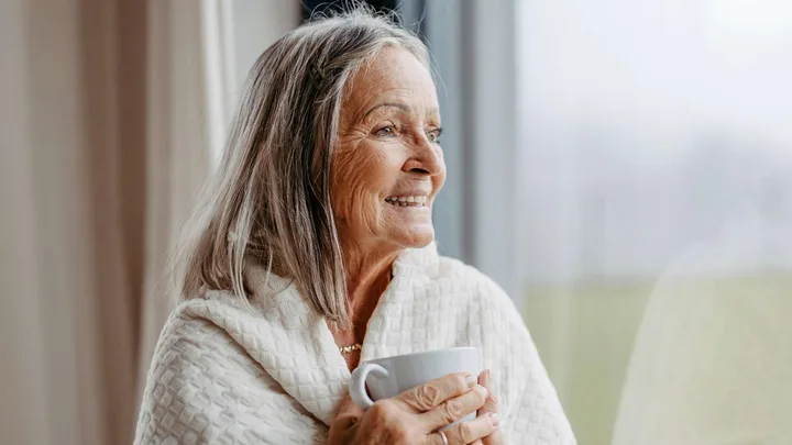A woman looking out of a window holding a warm mug