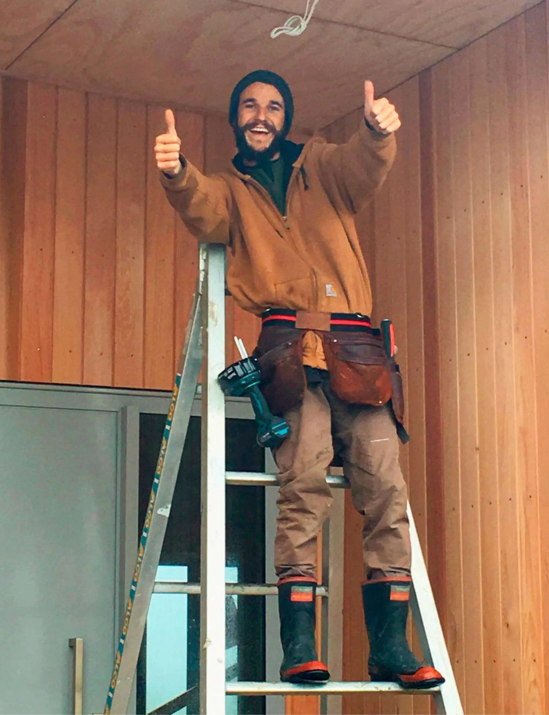 Traitors star Mike smiling and giving two thumbs up from the top of a ladder at work