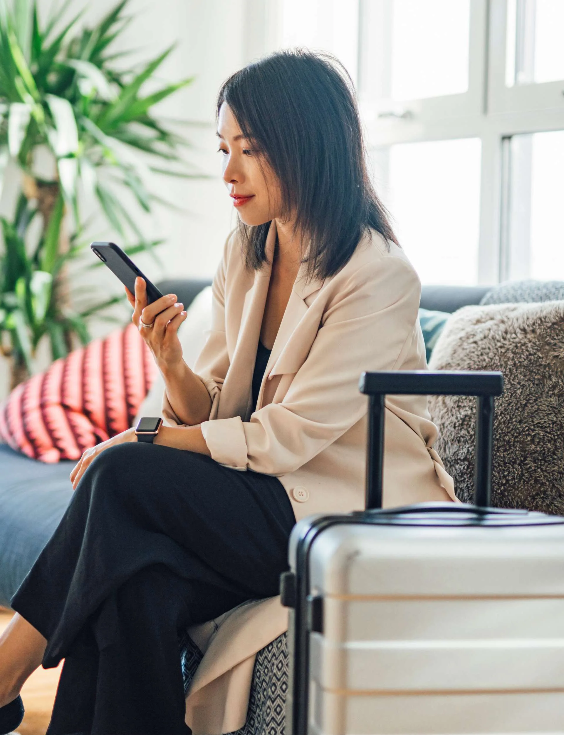 Woman looking at her phone while sitting beside her packed suitcase