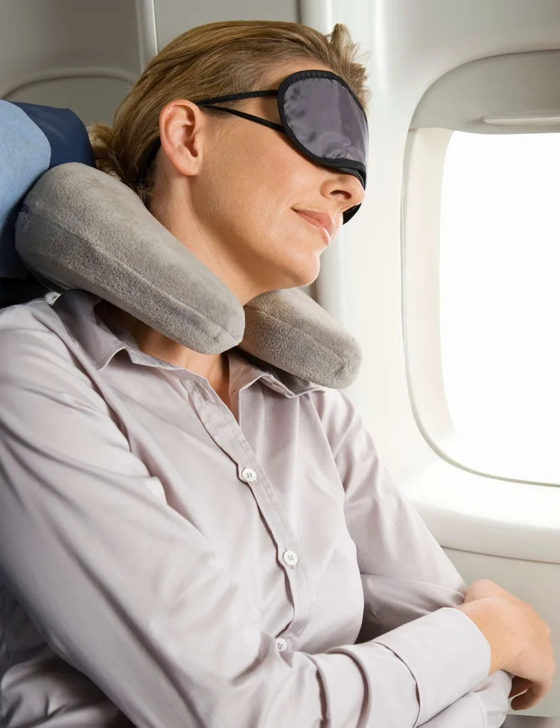 A woman flying economy with a neck pillow and eye mask