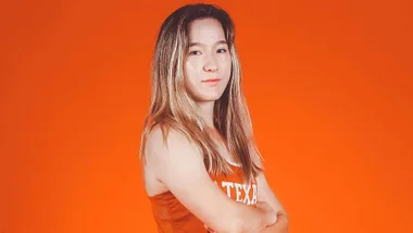 Lulu Sun in front of an orange background with her arms crossed
