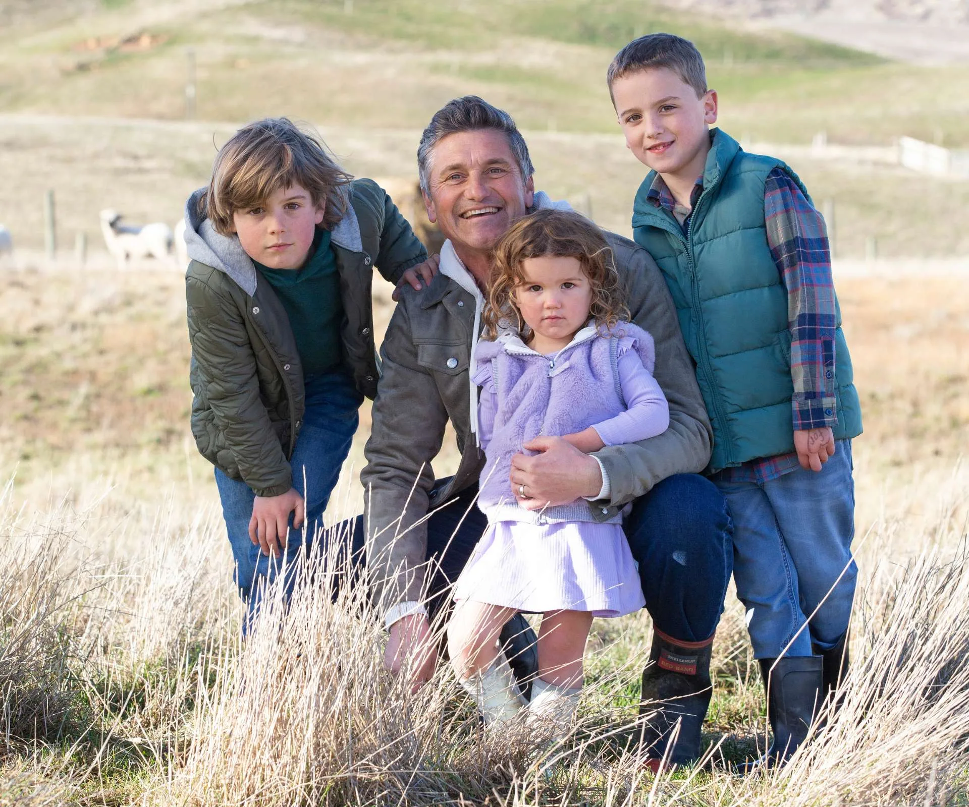 Matt Chisholm and his three kids crouching in the long grass on their farm