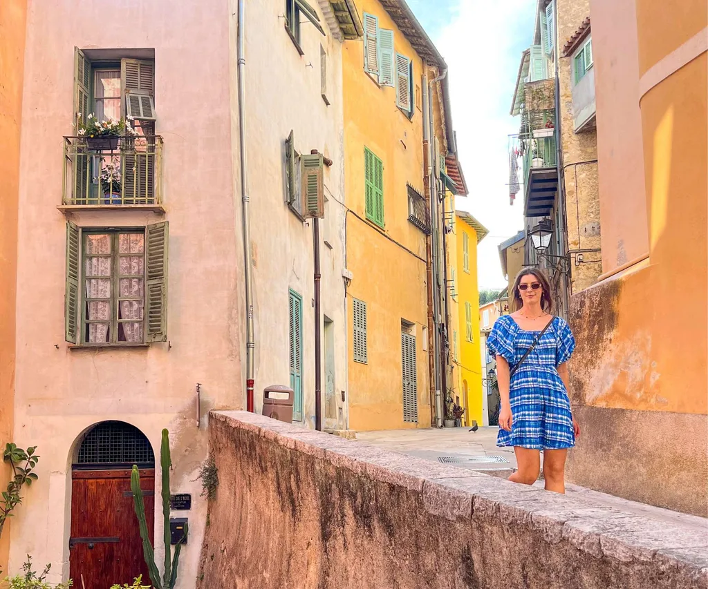 Jane Wills walking down a street in Sicily with large orange and pink buildings on either side