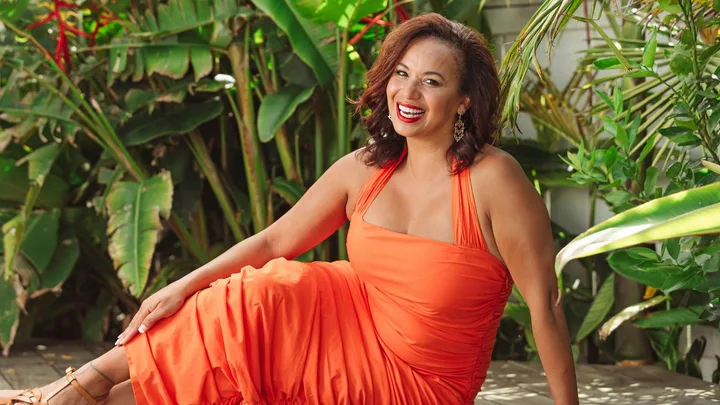 Megan Alatini leaning on her arm as she lays on her hip in an orange dress