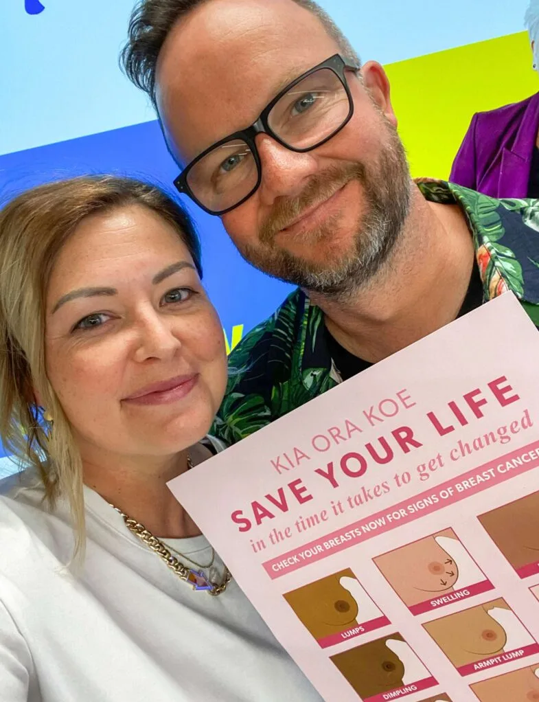 Sarah and Flynny taking a selfie, holding up a breast cancer awareness poster