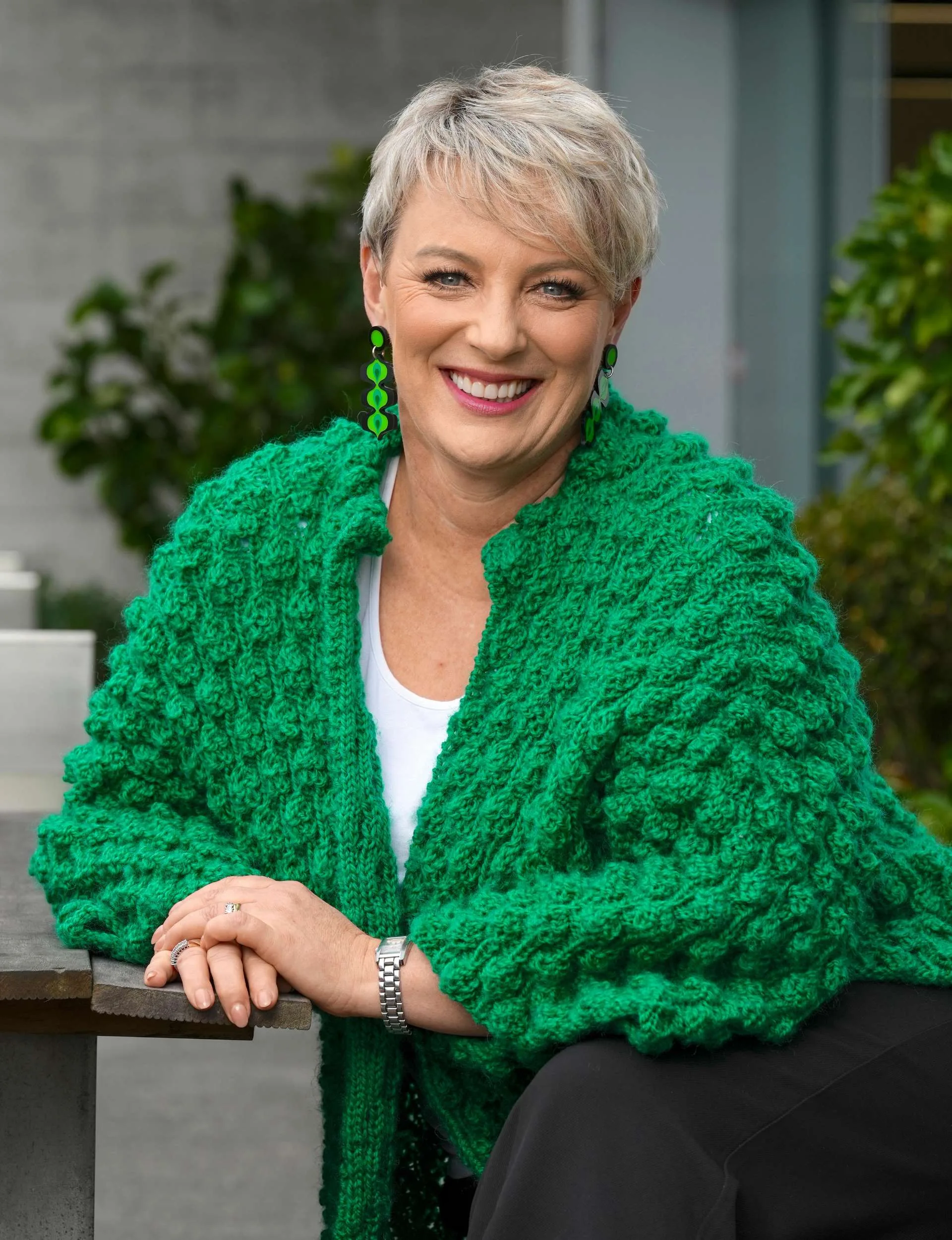 Lisa O'Neill smiling in a green-themed outfit - green jumper with dangling green earrings to match.
