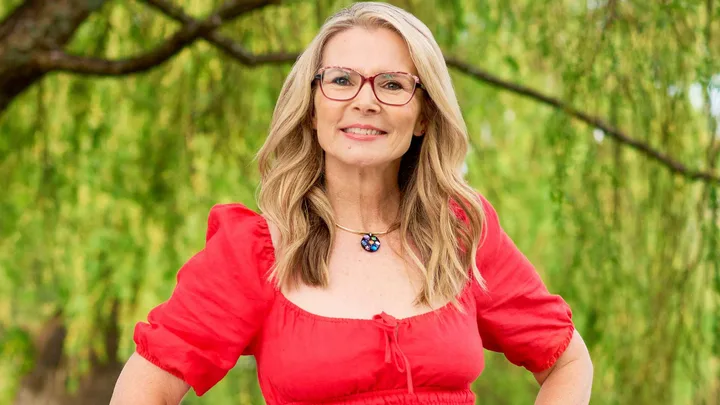 Suzy Cato smiling under a big tree in a red dress