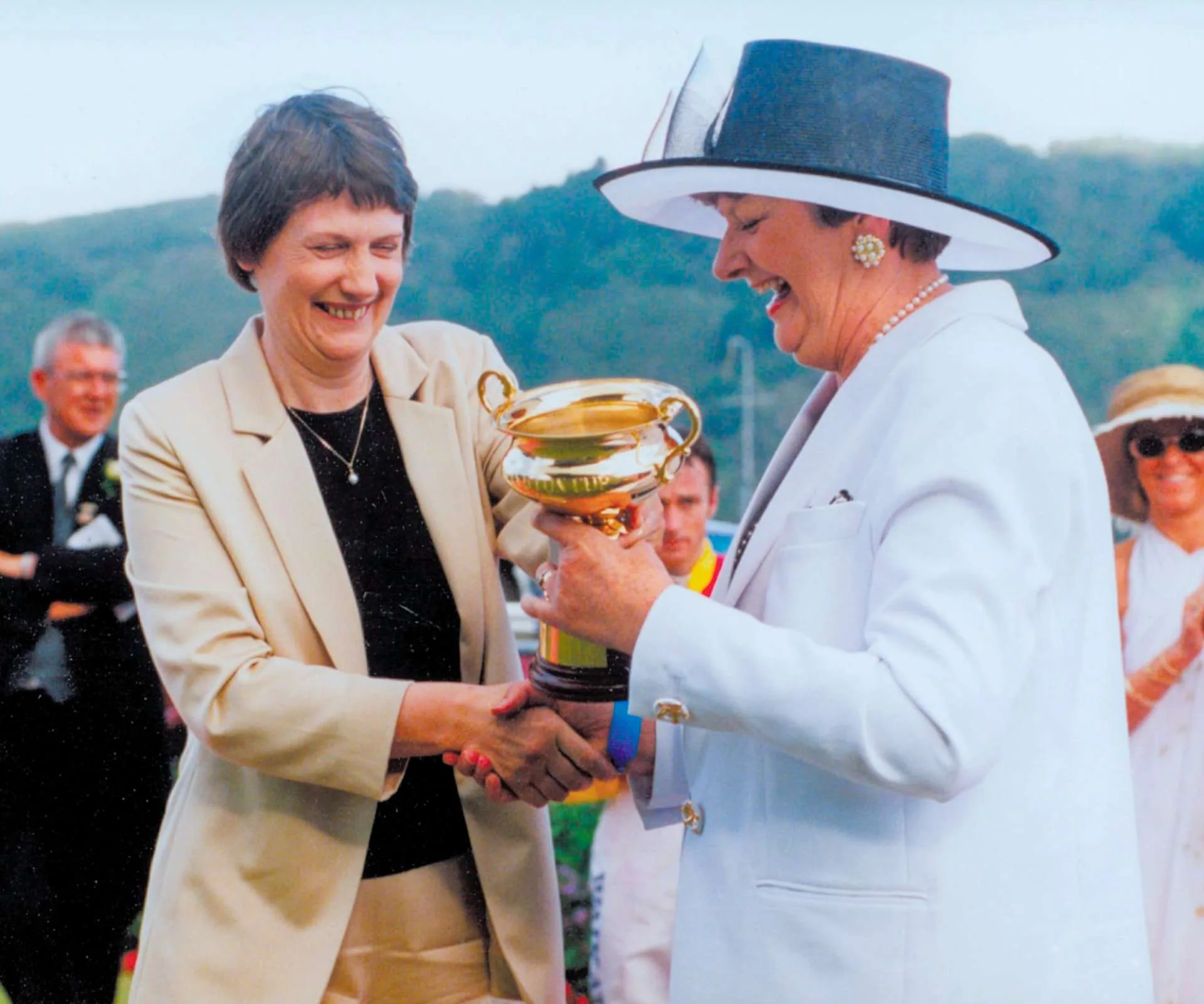 Dame Wendy Pye shaking hands and receiving a trophy from then-PM Helen Clark