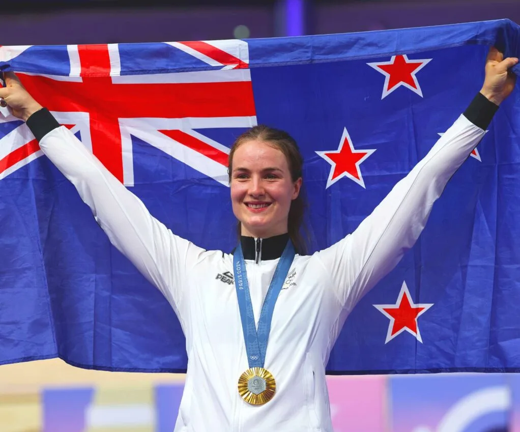 Ellesse Andrews holding an NZ flag up overhead after her 2024 Olympic win